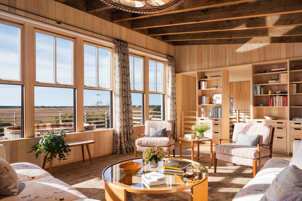 Imagen de sala de estar con biblioteca cerrada costera sin chimenea con paredes beige, suelo de madera clara y suelo beige