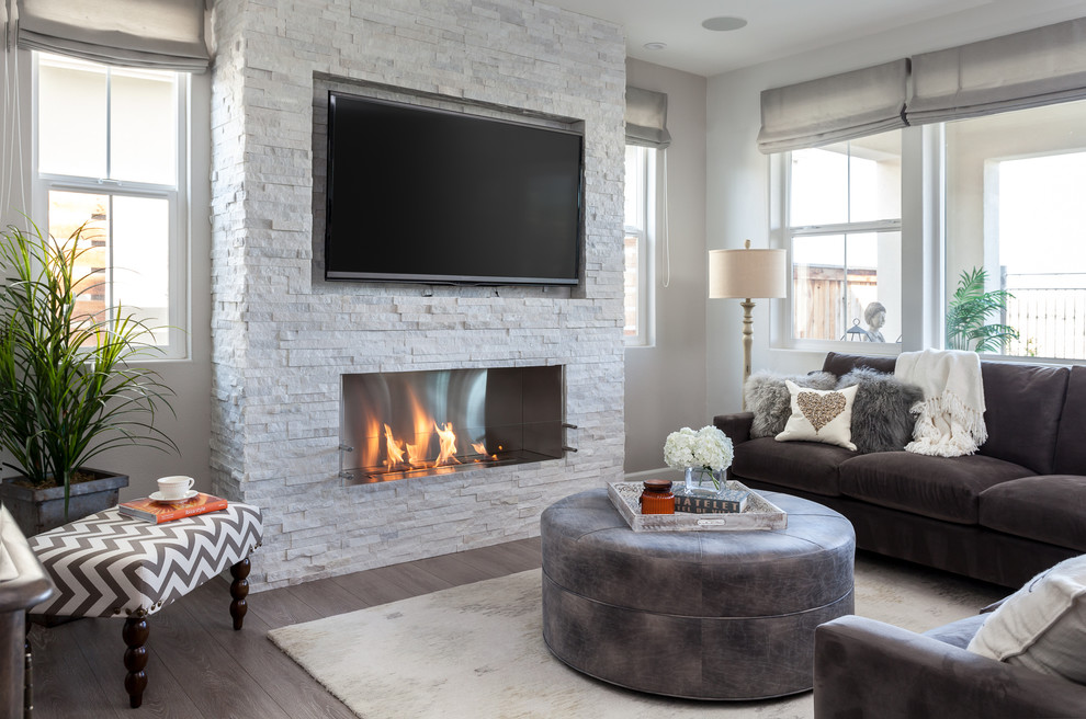 Diseño de sala de estar abierta clásica renovada de tamaño medio con paredes grises, suelo laminado, chimenea lineal, marco de chimenea de piedra y televisor colgado en la pared