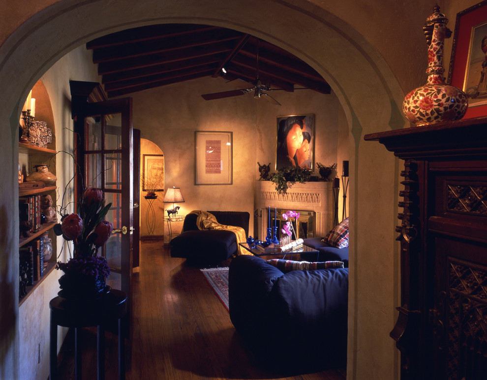 На фото: гостиная комната в средиземноморском стиле с бежевыми стенами, темным паркетным полом и угловым камином