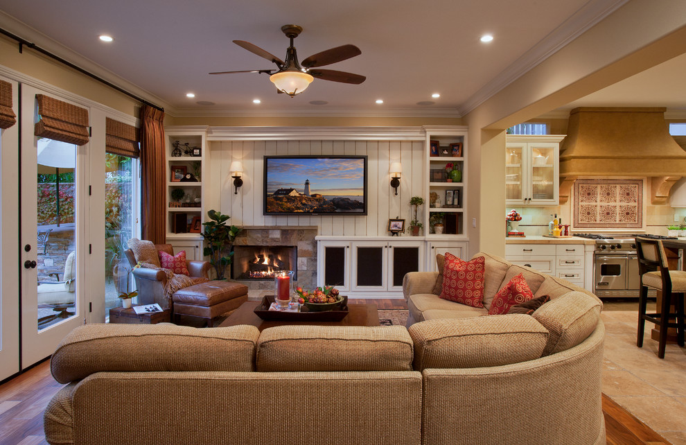 Inspiration for a large timeless open concept medium tone wood floor and brown floor family room remodel in Orange County with beige walls, a standard fireplace, a stone fireplace and a wall-mounted tv