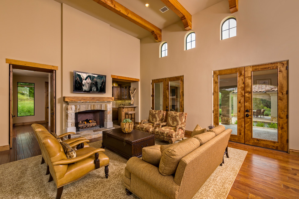 Foto de sala de estar abierta mediterránea grande con paredes beige, suelo de madera en tonos medios, todas las chimeneas, marco de chimenea de piedra y televisor colgado en la pared