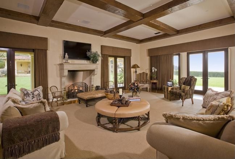 Photo of an expansive mediterranean open plan games room in Other with beige walls, carpet, a standard fireplace, a plastered fireplace surround, a wall mounted tv and beige floors.