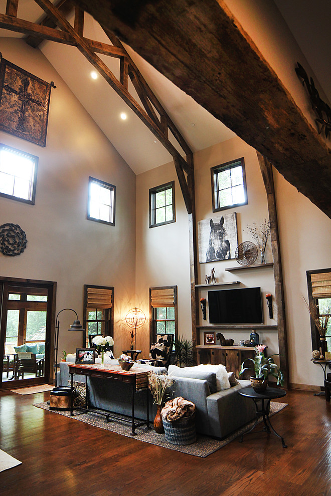 Modelo de sala de estar abierta de estilo de casa de campo grande con paredes beige, suelo de madera en tonos medios y televisor colgado en la pared