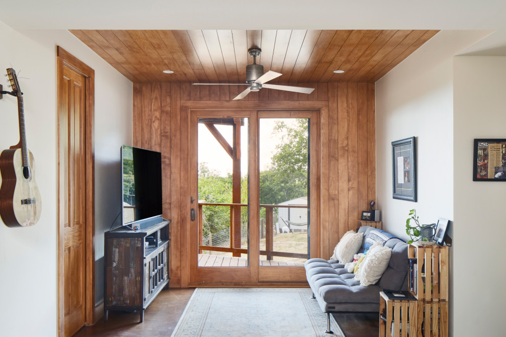 Diseño de sala de estar tropical con paredes blancas, suelo de cemento, televisor independiente, suelo marrón, madera y madera