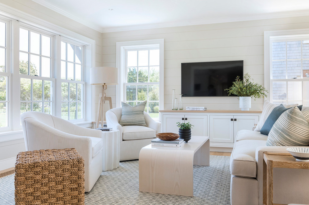 Imagen de sala de estar costera con paredes beige, suelo de madera en tonos medios, televisor colgado en la pared, suelo marrón y machihembrado