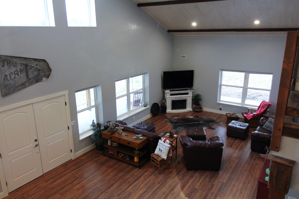Imagen de sala de juegos en casa abierta campestre grande con paredes grises, suelo de madera oscura, chimenea de esquina, televisor en una esquina y suelo marrón