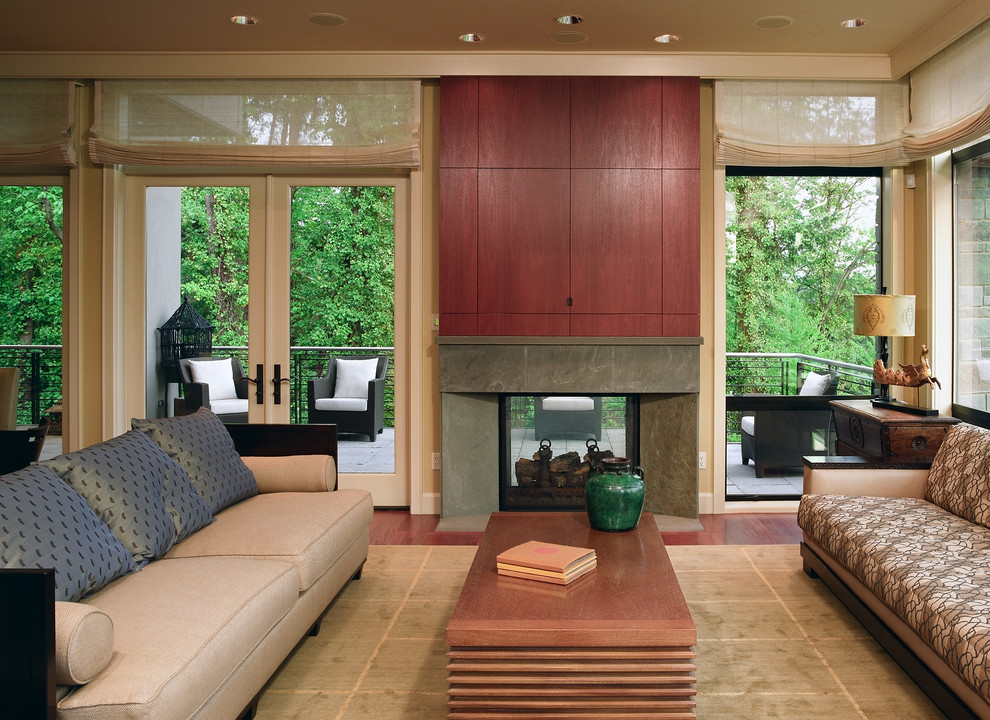 Ejemplo de sala de estar contemporánea con paredes beige, chimenea de doble cara, marco de chimenea de piedra y televisor retractable