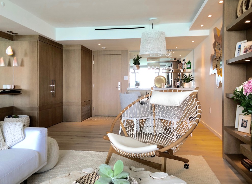 Modelo de sala de estar con barra de bar abierta moderna de tamaño medio sin chimenea con paredes blancas, suelo de madera clara, pared multimedia y suelo beige