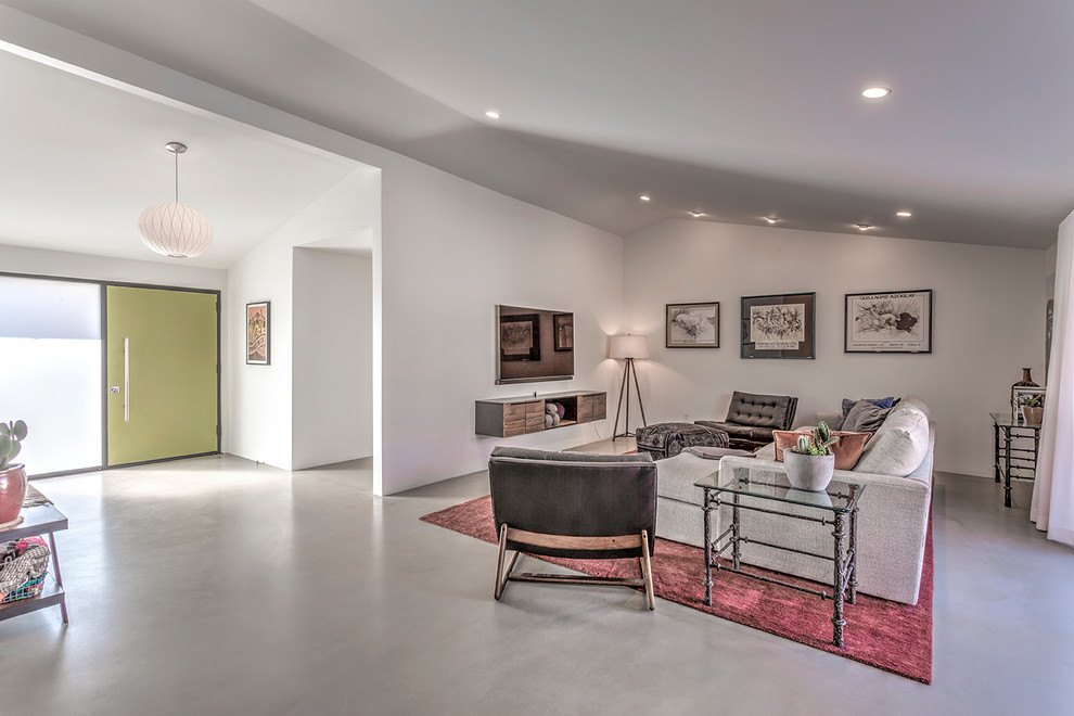 This is an example of a midcentury open plan games room in Phoenix with white walls, concrete flooring, a wall mounted tv and grey floors.