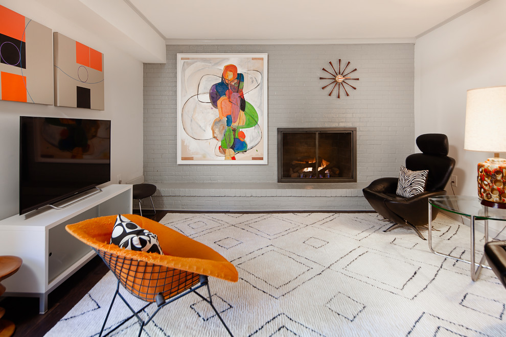 Mittelgroßes Mid-Century Wohnzimmer mit dunklem Holzboden, Kamin, Kaminumrandung aus Backstein, grauer Wandfarbe und freistehendem TV in Charlotte