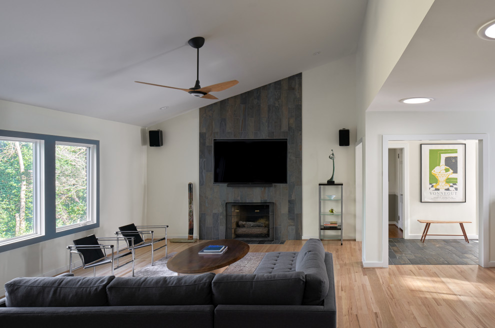 Exemple d'une salle de séjour rétro de taille moyenne et ouverte avec un mur blanc, un sol en bois brun, une cheminée standard, un manteau de cheminée en pierre, un téléviseur fixé au mur et un sol marron.