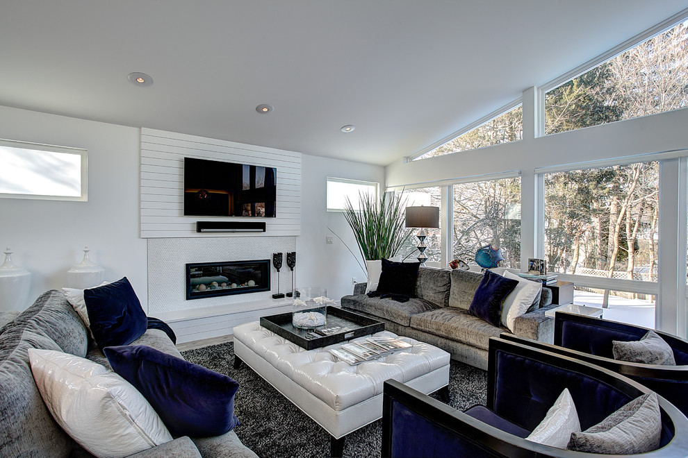 Diseño de sala de estar abierta actual grande con paredes blancas, suelo de madera clara, chimenea lineal, marco de chimenea de piedra y televisor colgado en la pared