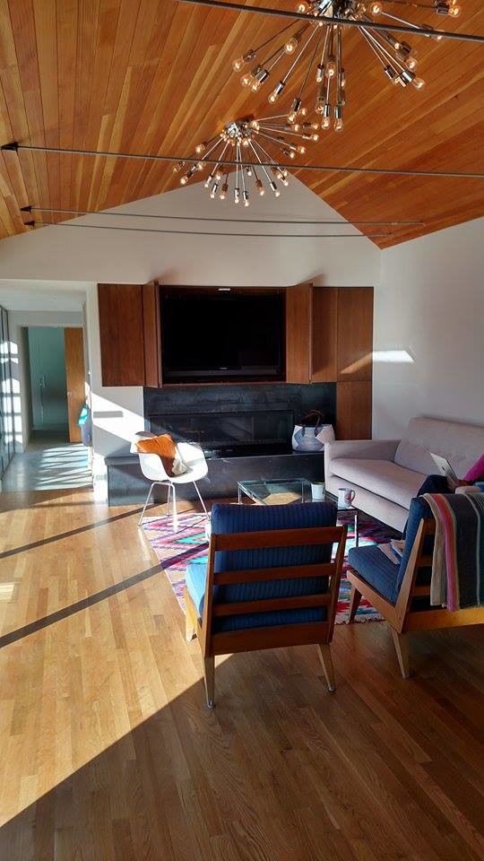 Modelo de sala de estar abierta retro con paredes blancas, suelo de madera clara, todas las chimeneas, marco de chimenea de metal y televisor retractable
