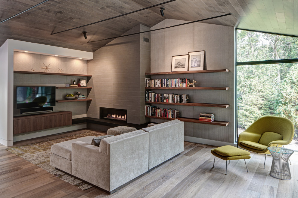 Foto di un soggiorno minimalista aperto con libreria, pareti grigie, parquet chiaro, camino lineare Ribbon, cornice del camino piastrellata e TV a parete