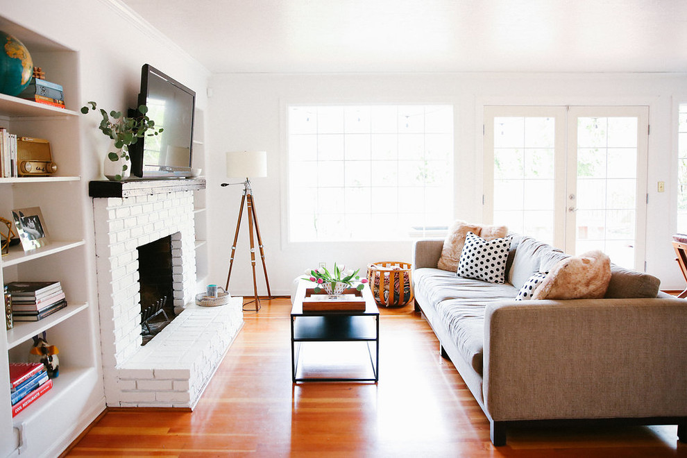 Mittelgroßes, Offenes Mid-Century Wohnzimmer mit weißer Wandfarbe, braunem Holzboden, Kamin, Kaminumrandung aus Backstein, TV-Wand und braunem Boden in Portland