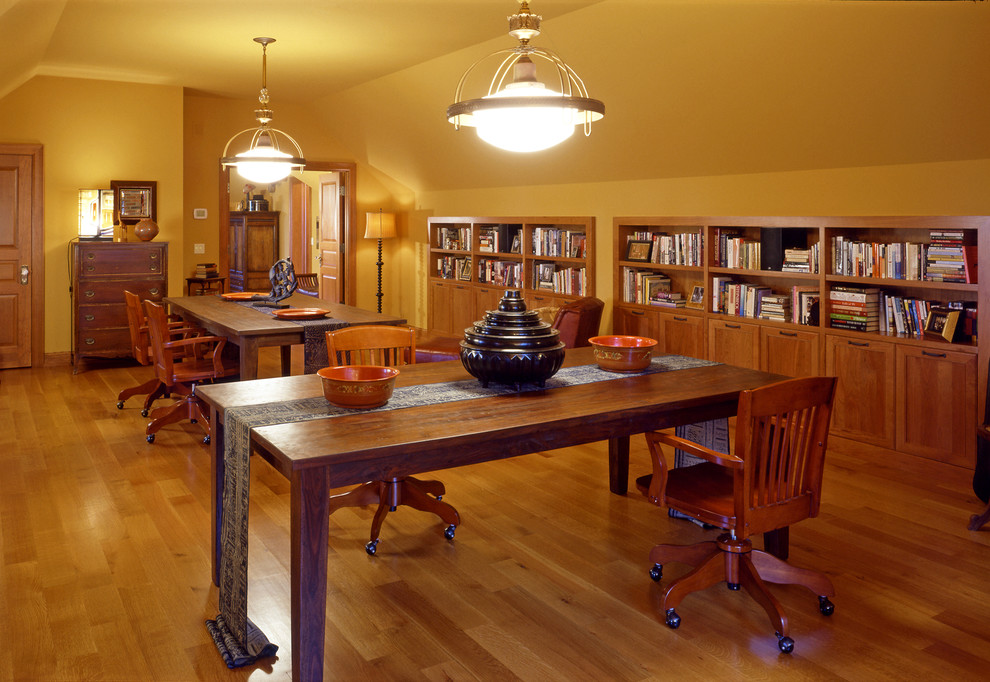 Foto på ett mycket stort vintage arbetsrum, med ett bibliotek, gula väggar och mellanmörkt trägolv