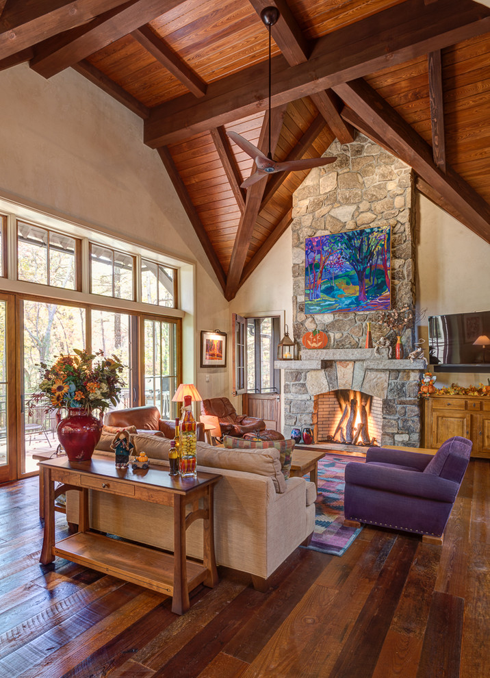 Diseño de sala de estar abierta rural de tamaño medio con paredes beige, suelo de madera en tonos medios, todas las chimeneas, marco de chimenea de piedra y televisor colgado en la pared