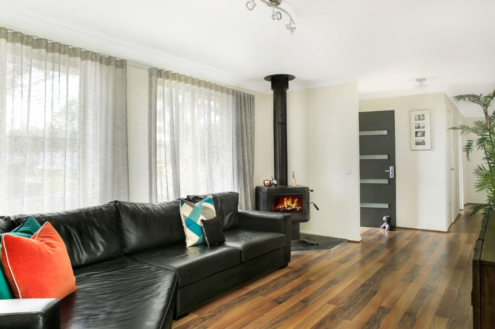 Kleines, Abgetrenntes Landhaus Wohnzimmer mit weißer Wandfarbe, braunem Holzboden, Eckkamin, Kaminumrandung aus Metall, TV-Wand und buntem Boden in Wollongong
