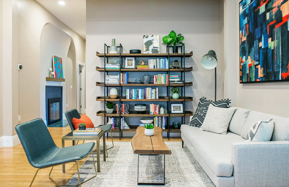 Immagine di un soggiorno design aperto con libreria, pareti grigie, parquet chiaro, nessuna TV e pavimento beige