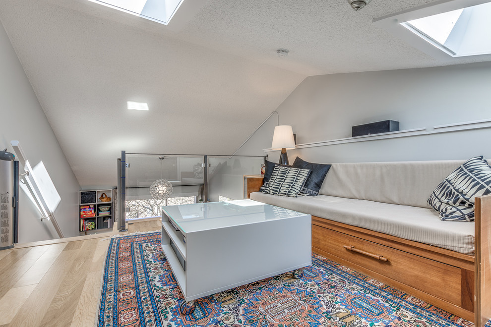 Cette image montre une petite salle de séjour mansardée ou avec mezzanine minimaliste avec un mur gris, parquet clair, aucune cheminée, un téléviseur fixé au mur et un sol beige.