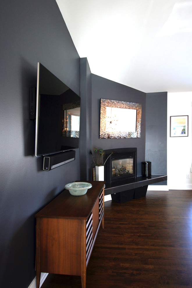 Ejemplo de sala de estar abierta retro de tamaño medio con paredes grises, suelo de madera en tonos medios, todas las chimeneas, marco de chimenea de yeso y televisor colgado en la pared