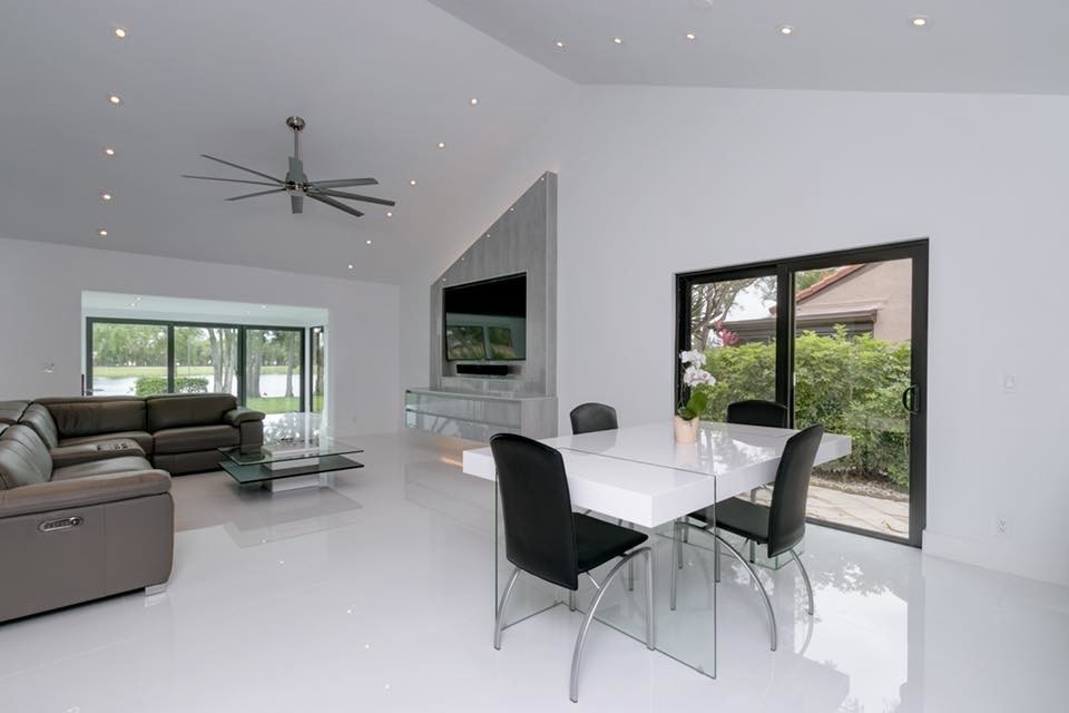 Modelo de sala de estar abierta minimalista grande sin chimenea con paredes blancas, suelo de cemento, televisor colgado en la pared y suelo blanco