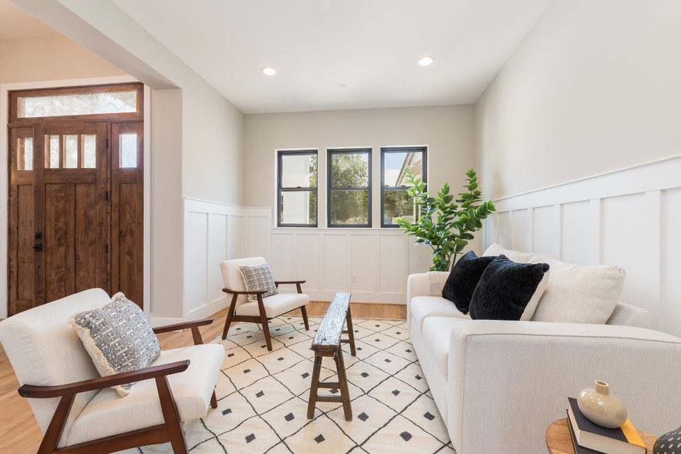 Imagen de sala de estar abierta de estilo de casa de campo de tamaño medio sin chimenea y televisor con paredes beige, suelo de madera clara, suelo beige y boiserie