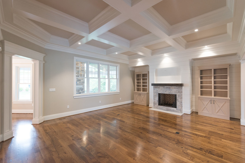 Cette photo montre une salle de séjour craftsman ouverte avec un mur gris, un sol en bois brun, une cheminée standard, un manteau de cheminée en pierre, un téléviseur fixé au mur et un sol marron.
