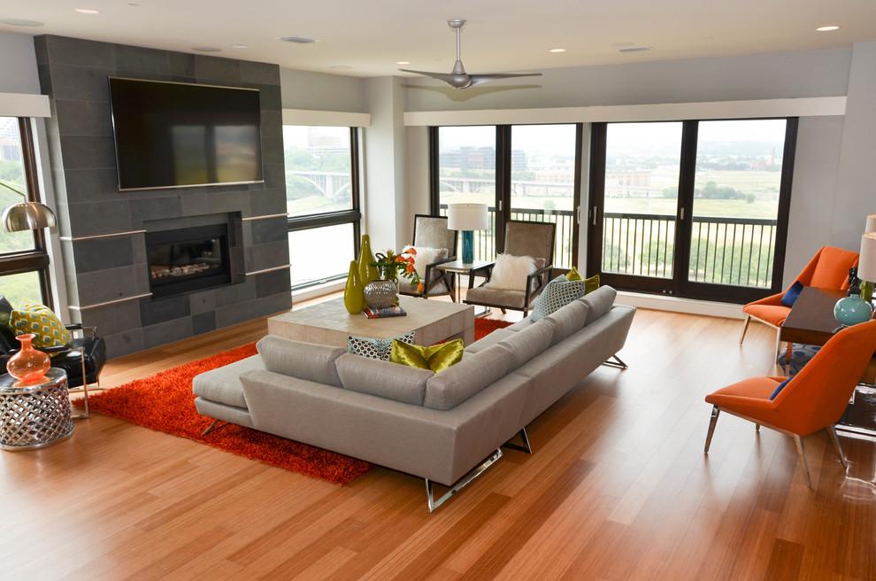 Стильный дизайн: большая двухуровневая гостиная комната в современном стиле с серыми стенами, полом из бамбука, стандартным камином, телевизором на стене, фасадом камина из камня, оранжевым полом и ковром на полу - последний тренд
