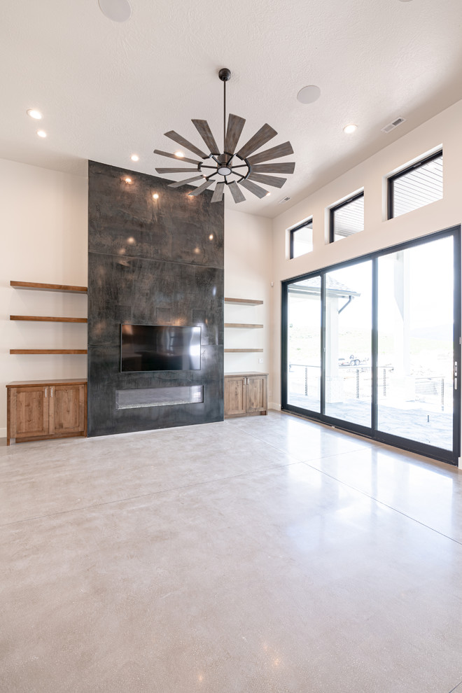 This is an example of a large country open plan games room in Salt Lake City with grey walls, concrete flooring, a standard fireplace, a metal fireplace surround, a wall mounted tv and grey floors.