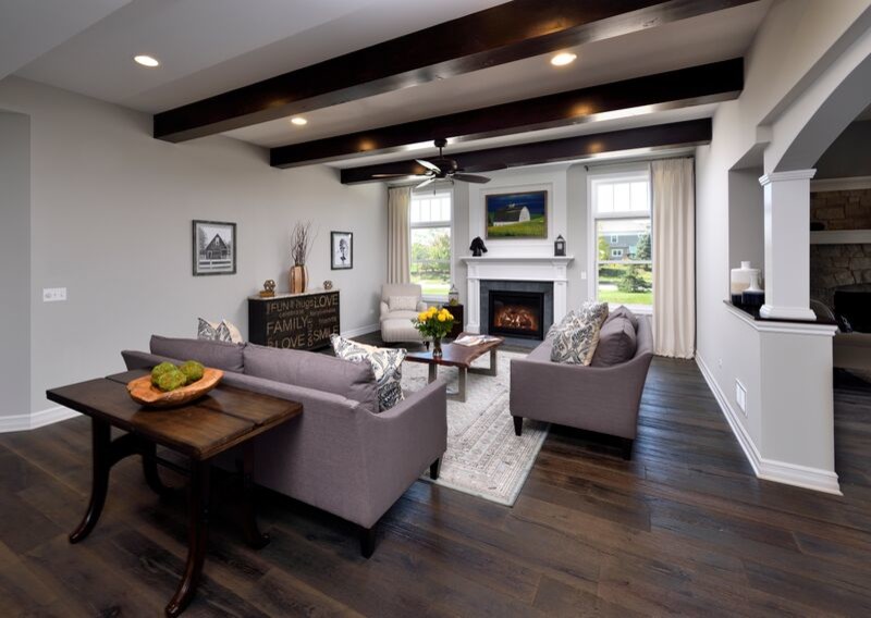 Imagen de sala de estar abierta de estilo de casa de campo grande con paredes grises, suelo de madera oscura, todas las chimeneas, marco de chimenea de piedra y televisor colgado en la pared