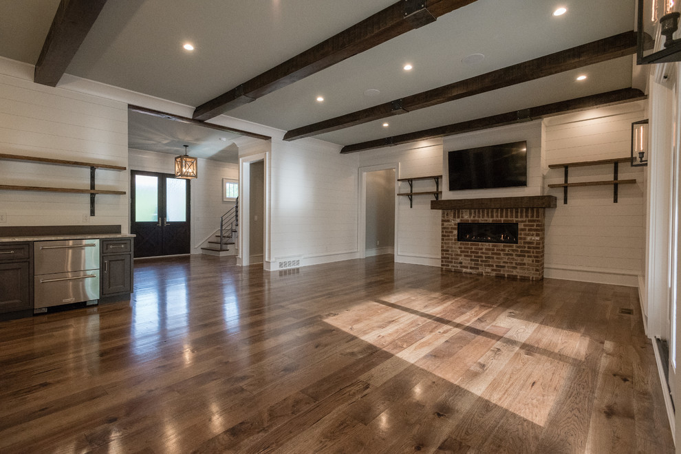 This is an example of a medium sized rural open plan games room in Atlanta with white walls, dark hardwood flooring, a wall mounted tv, brown floors, a ribbon fireplace and a brick fireplace surround.