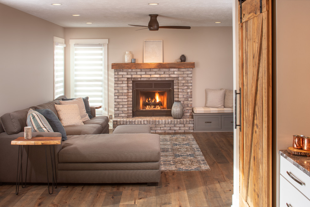 Modelo de sala de estar con barra de bar abierta de estilo de casa de campo de tamaño medio con paredes grises, suelo de madera en tonos medios, todas las chimeneas, marco de chimenea de ladrillo y suelo marrón