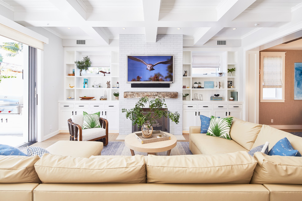 Modelo de sala de estar marinera con paredes blancas, suelo de madera en tonos medios, todas las chimeneas, marco de chimenea de ladrillo, televisor colgado en la pared y suelo marrón