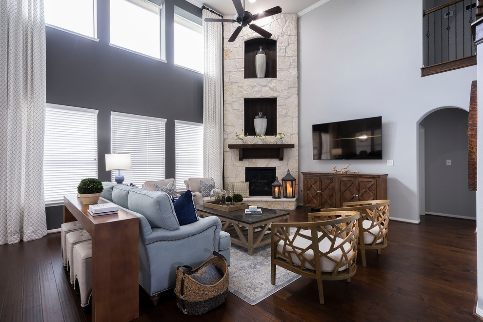Ejemplo de sala de estar costera con paredes grises, suelo de madera oscura, chimenea de esquina, marco de chimenea de piedra, televisor colgado en la pared y suelo marrón