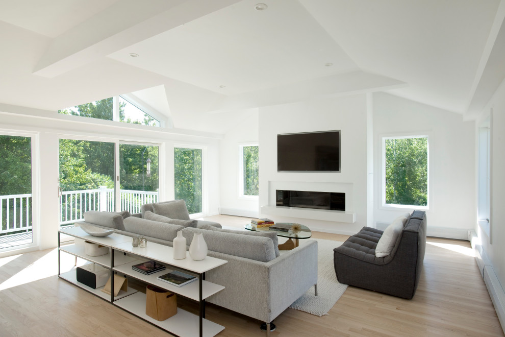Foto de sala de estar abierta y abovedada moderna de tamaño medio con paredes blancas, suelo de madera clara, todas las chimeneas, marco de chimenea de yeso y televisor colgado en la pared