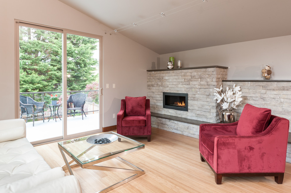 Diseño de sala de estar abierta moderna pequeña con paredes grises, suelo de madera clara, chimenea lineal y marco de chimenea de piedra