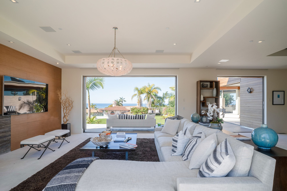 Modelo de sala de estar abierta costera grande con paredes blancas, suelo de travertino, televisor colgado en la pared y suelo blanco