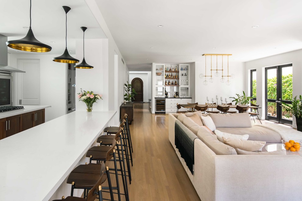 This is an example of a large modern open plan living room in Los Angeles with white walls, medium hardwood flooring, a standard fireplace, a stone fireplace surround, a wall mounted tv, beige floors and a home bar.