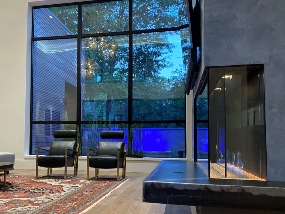 Expansive modern open plan games room in Houston with white walls, light hardwood flooring, a two-sided fireplace, a metal fireplace surround, a wall mounted tv and a drop ceiling.