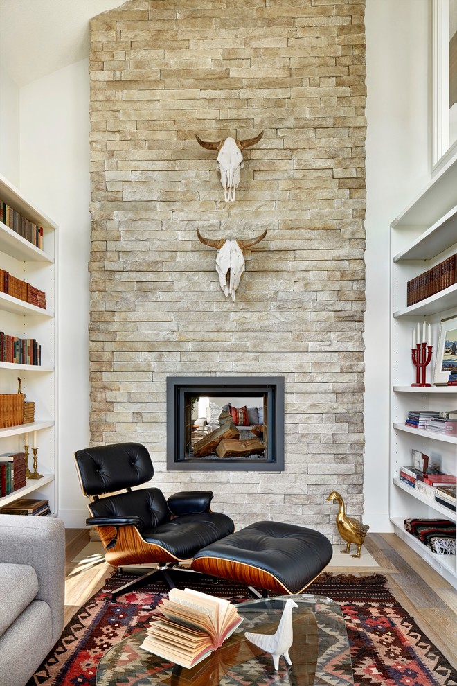 Imagen de sala de estar con biblioteca abierta de estilo de casa de campo extra grande con paredes blancas, chimenea de doble cara, marco de chimenea de piedra y suelo de madera en tonos medios