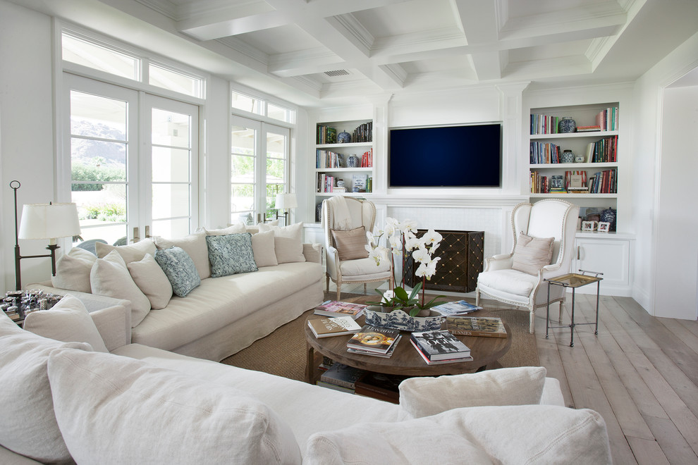 На фото: гостиная комната в стиле неоклассика (современная классика) с с книжными шкафами и полками, белыми стенами, светлым паркетным полом, стандартным камином и телевизором на стене