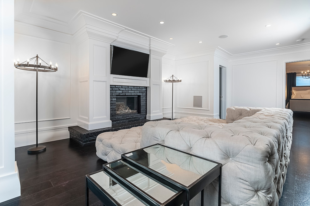 Large modern enclosed games room in Edmonton with white walls, dark hardwood flooring, a standard fireplace, a brick fireplace surround and a wall mounted tv.