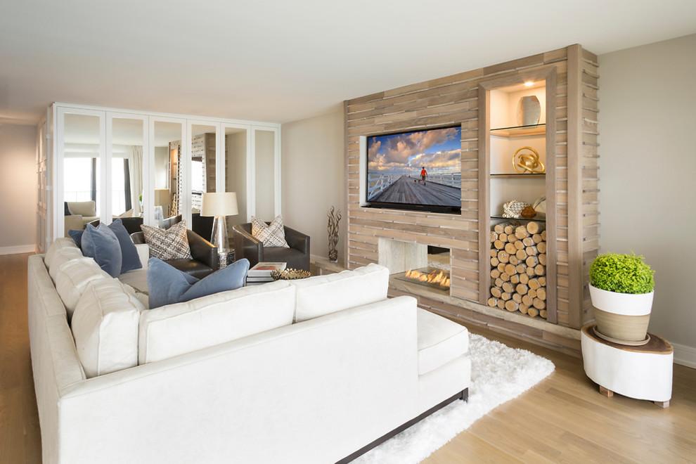 Imagen de sala de estar costera con paredes beige, suelo de madera clara, chimenea de doble cara, marco de chimenea de baldosas y/o azulejos, televisor colgado en la pared y suelo beige