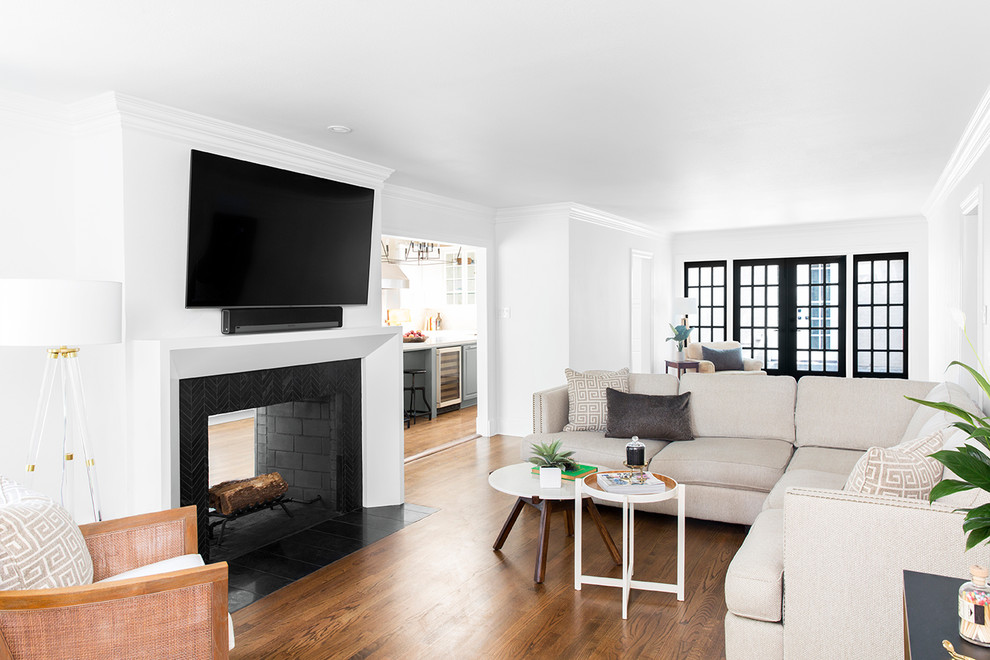 Пример оригинального дизайна: изолированная гостиная комната среднего размера в стиле неоклассика (современная классика) с белыми стенами, паркетным полом среднего тона, двусторонним камином, фасадом камина из плитки, телевизором на стене и коричневым полом