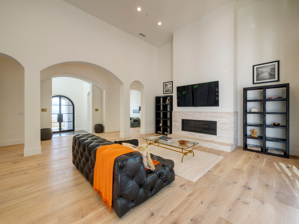 Ejemplo de sala de estar abierta minimalista extra grande con paredes blancas, suelo de madera clara, todas las chimeneas, marco de chimenea de piedra y televisor colgado en la pared