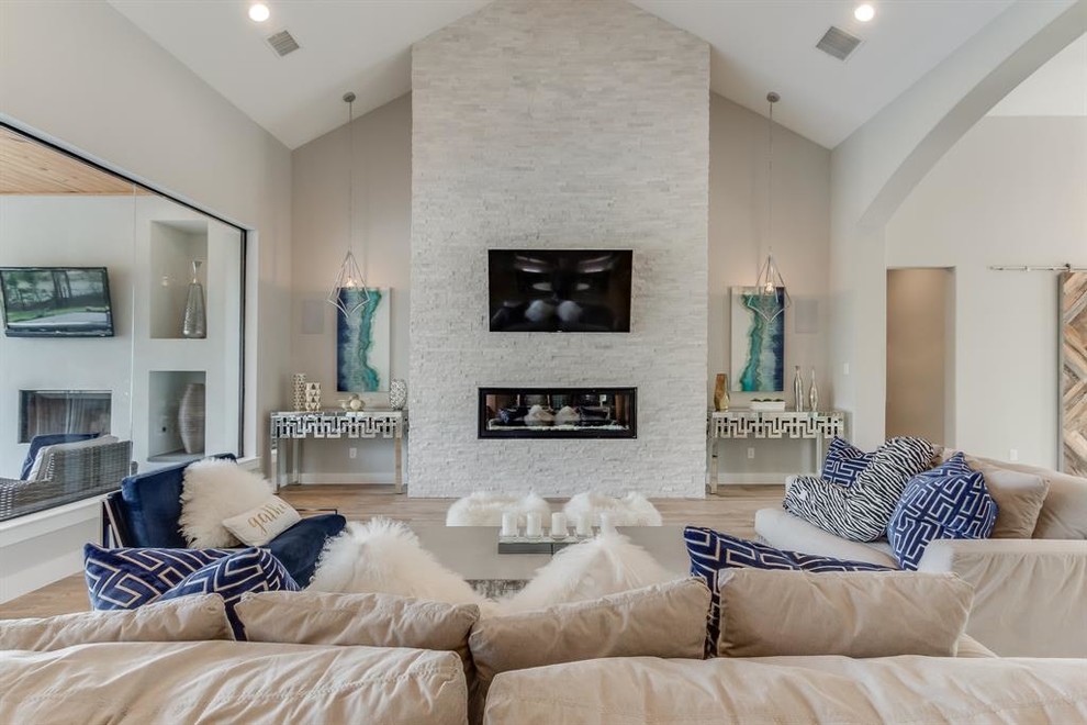 Imagen de sala de estar abierta moderna grande con paredes beige, suelo de madera clara, chimenea lineal, marco de chimenea de piedra, televisor colgado en la pared y suelo beige