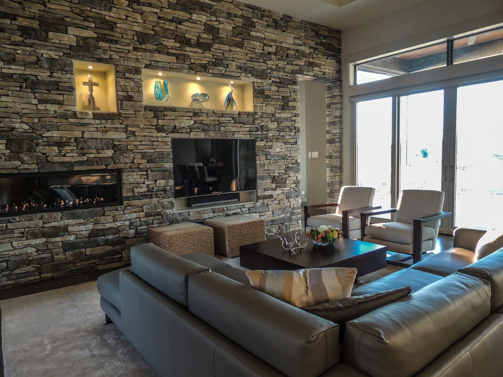 На фото: большая открытая гостиная комната в современном стиле с серыми стенами, бетонным полом, горизонтальным камином, фасадом камина из камня, телевизором на стене и коричневым полом с