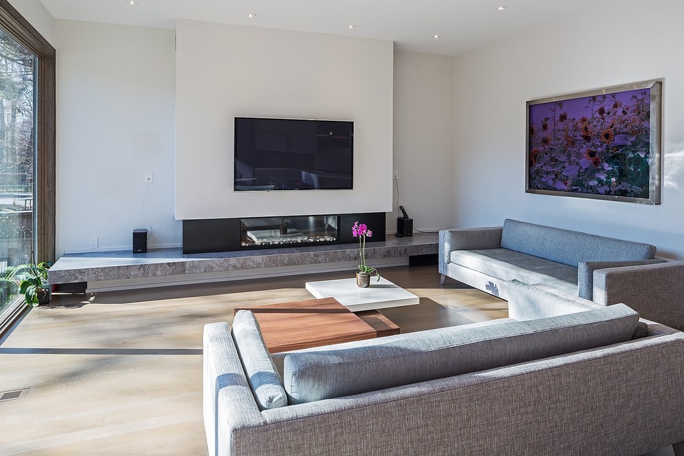 Modelo de sala de estar abierta moderna grande con paredes blancas, suelo de madera en tonos medios, chimenea lineal, televisor colgado en la pared, marco de chimenea de metal y suelo marrón