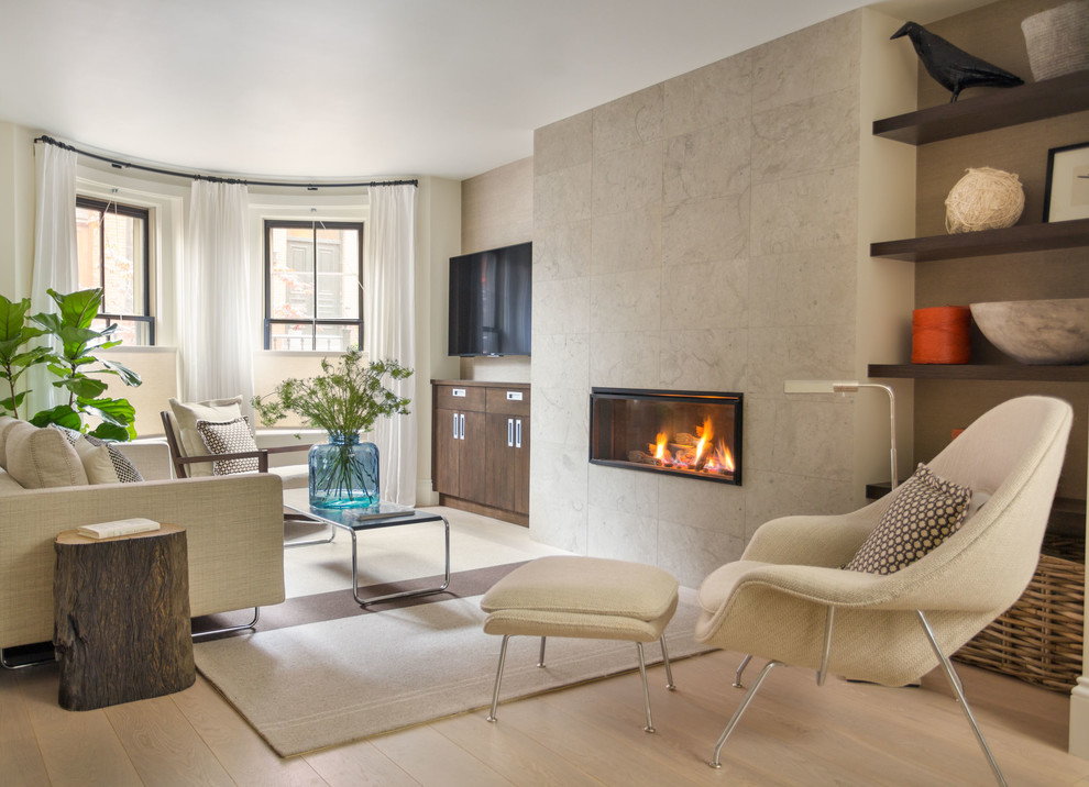 Modelo de sala de estar actual con suelo de madera clara, chimeneas suspendidas, marco de chimenea de piedra y televisor colgado en la pared
